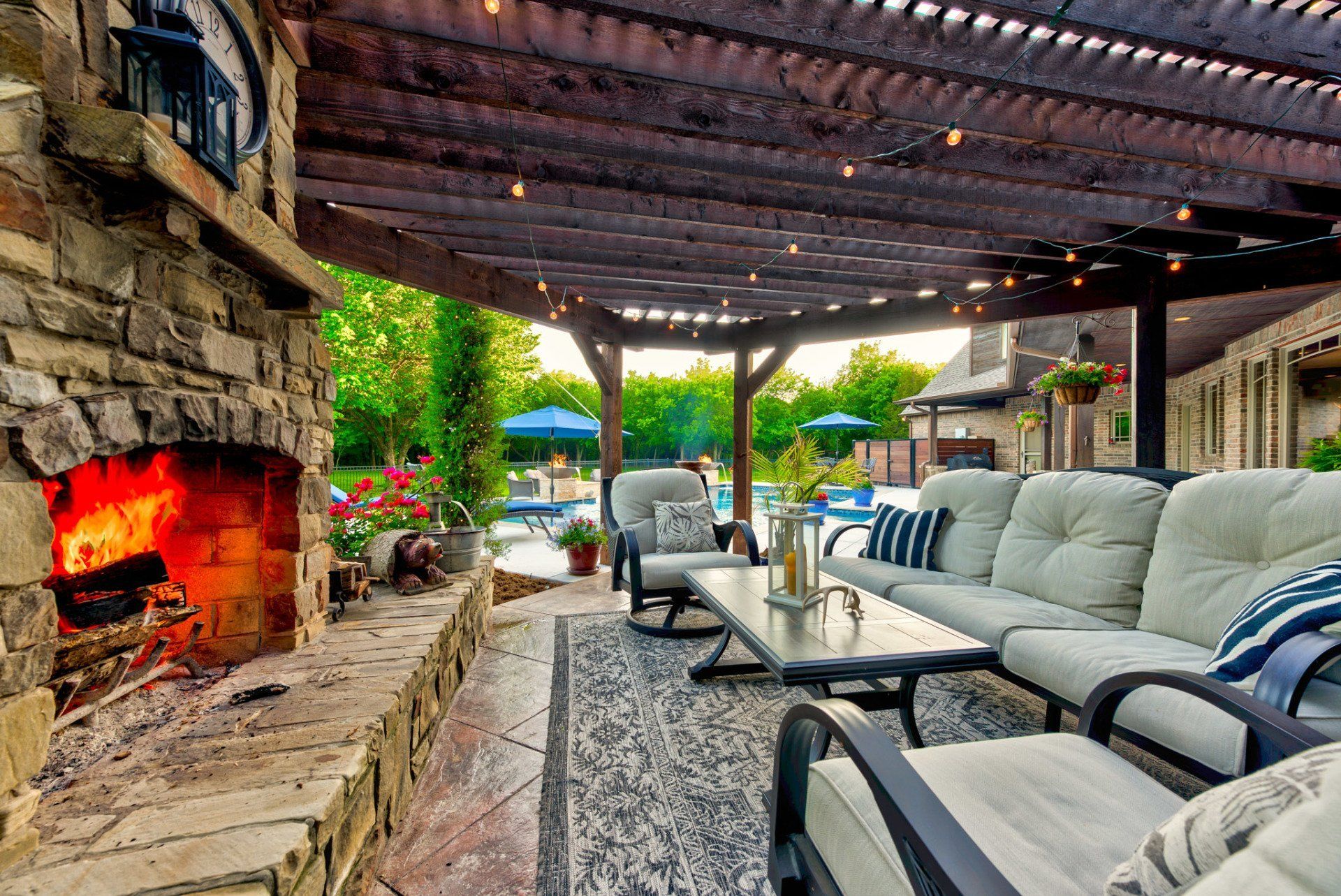 A patio with a fireplace and a couch and chairs under a pergola.