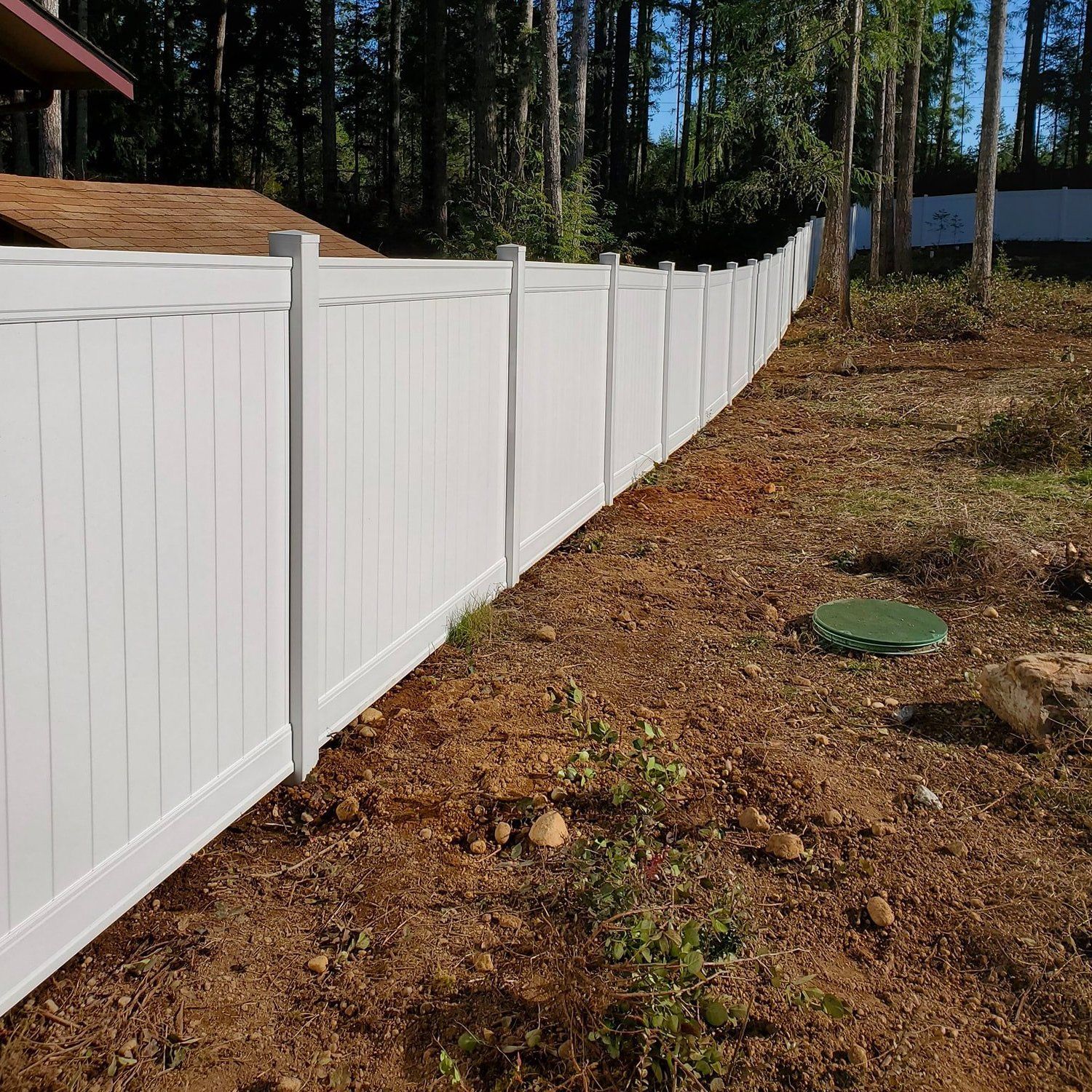 White vinyl fence in a wooded area.