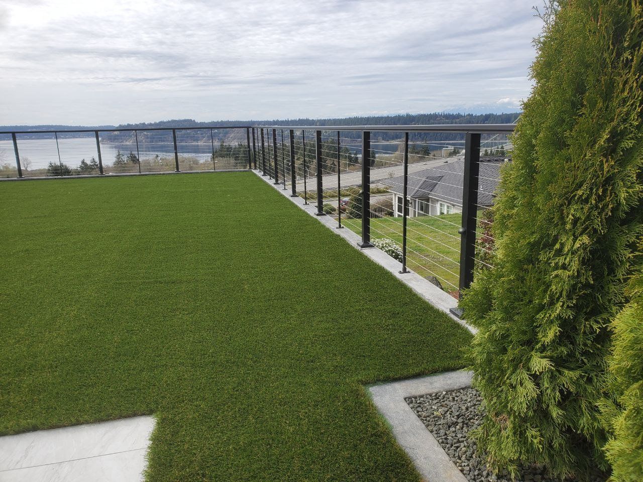Rooftop patio with green turf, metal railing, and view of water and sky.