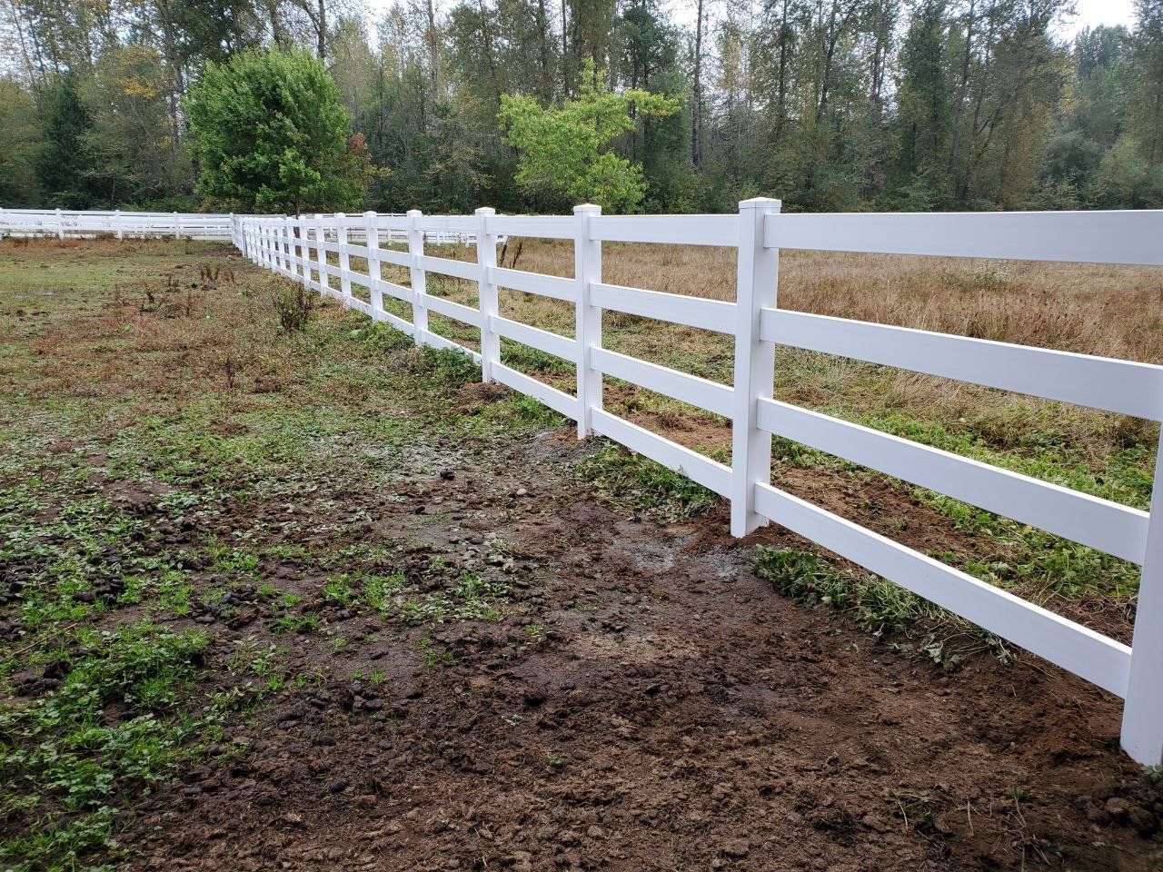 White vinyl fence in a field with trees in the background.