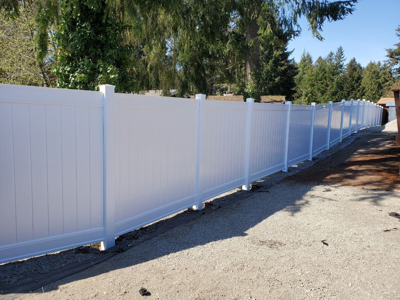 White vinyl fence along a gravel driveway, sunny day.