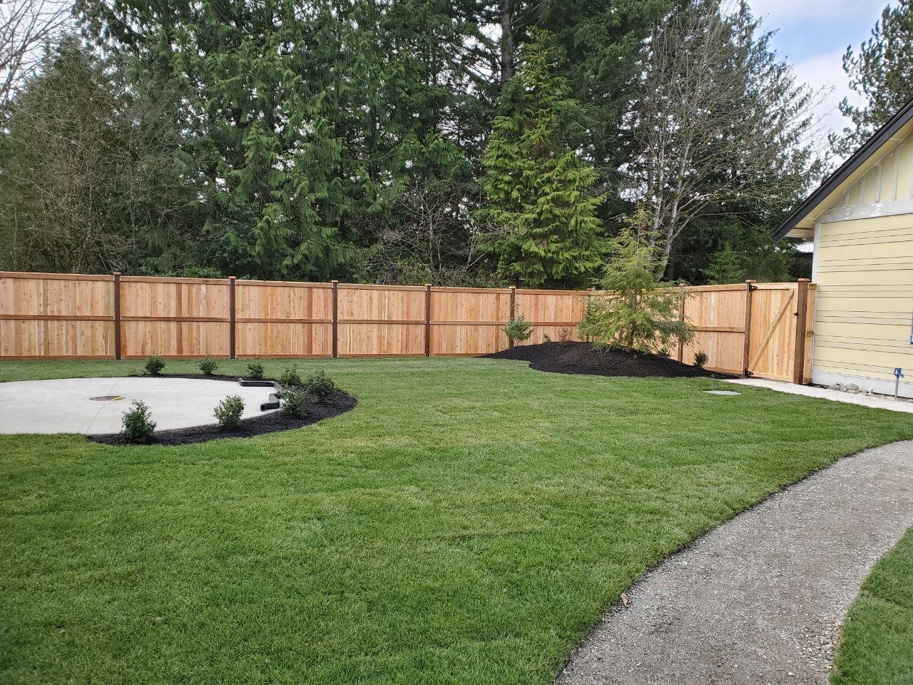 A backyard with green grass, a wooden fence, and a gravel pathway.