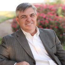 A man in a suit and white shirt is sitting down and smiling.