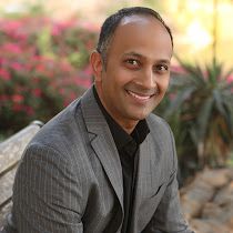 A man in a suit is sitting on a bench and smiling.