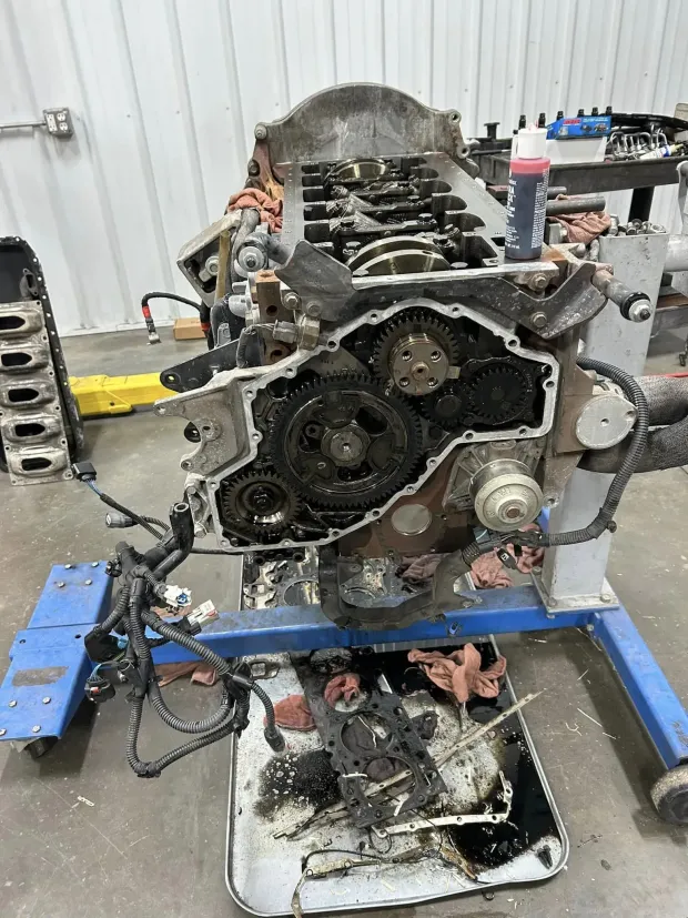 A disassembled automotive engine on a blue metal stand in a workshop, with internal gears and parts exposed.