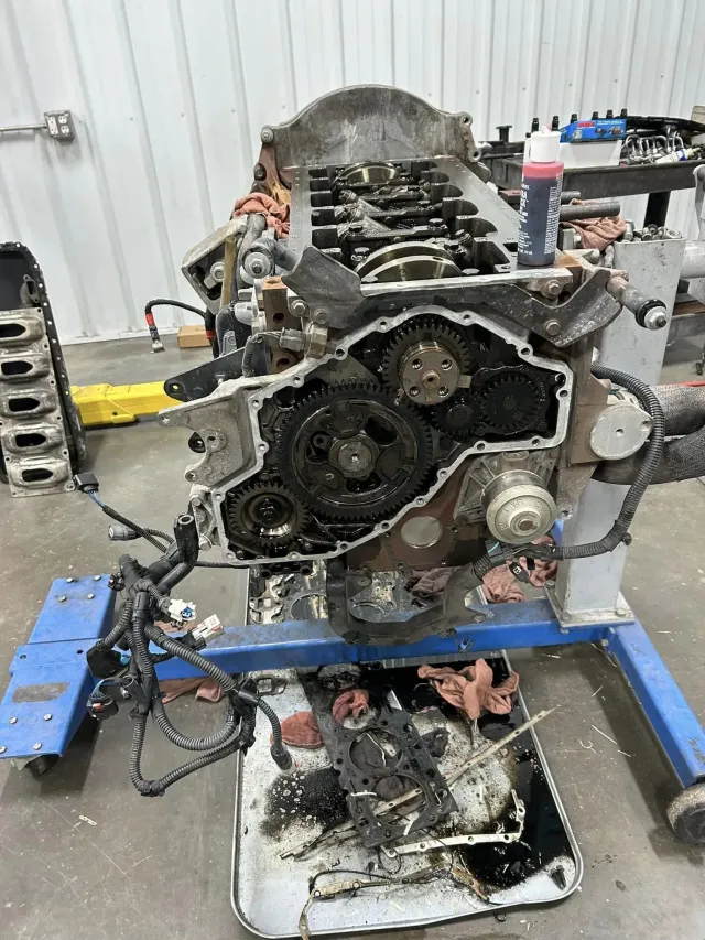 An automotive engine block mounted on a blue stand in a workshop, with internal gears and components exposed.