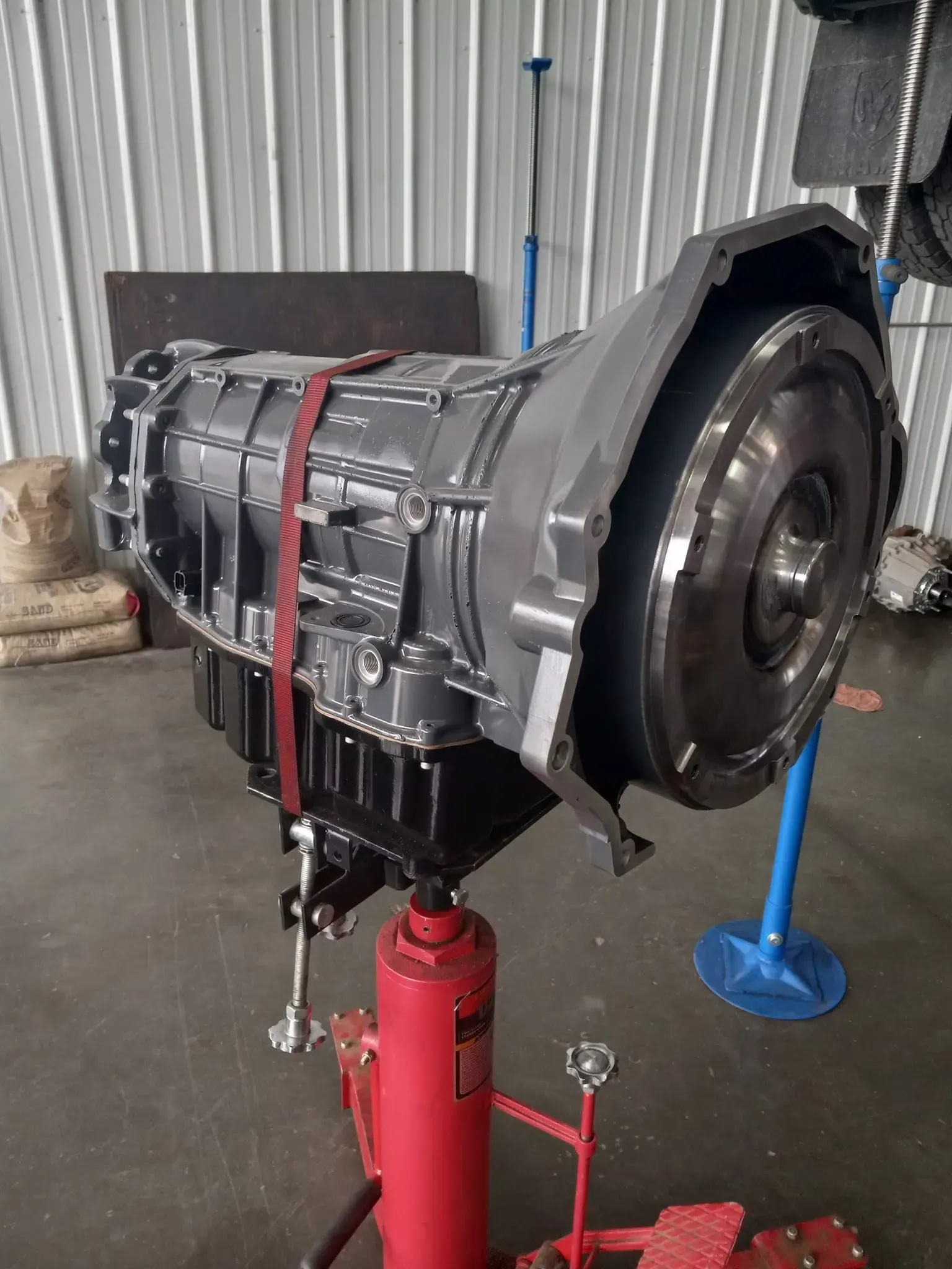 A car transmission secured on a red hydraulic shop jack in a garage.