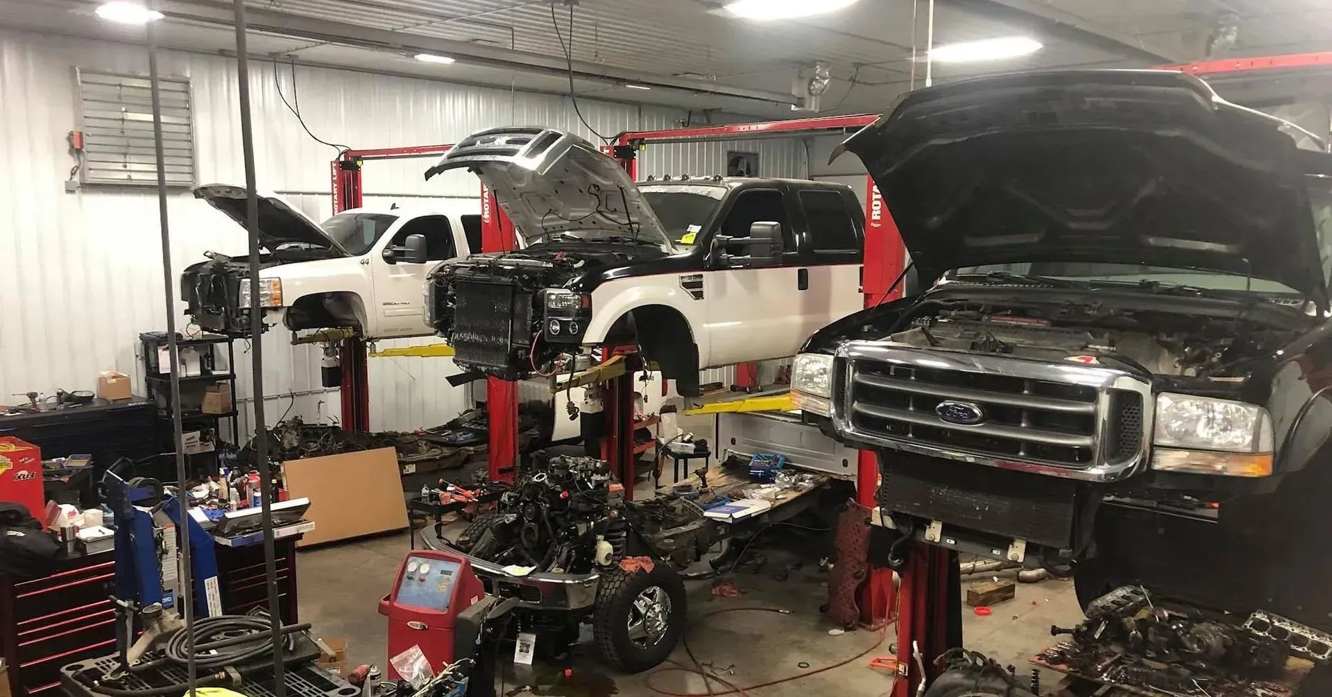 Auto repair shop with several pickup trucks elevated on hydraulic lifts for engine maintenance.