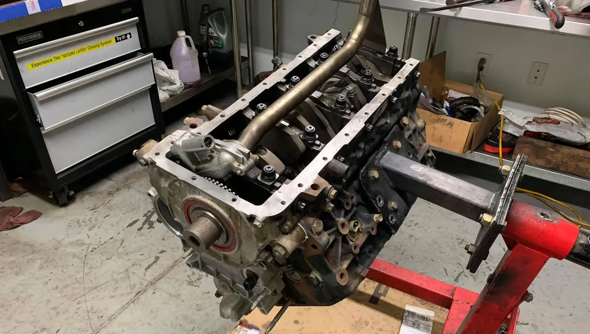 An automotive engine block mounted on a red metal stand in a workshop, showing the internal components and oil pickup tube.