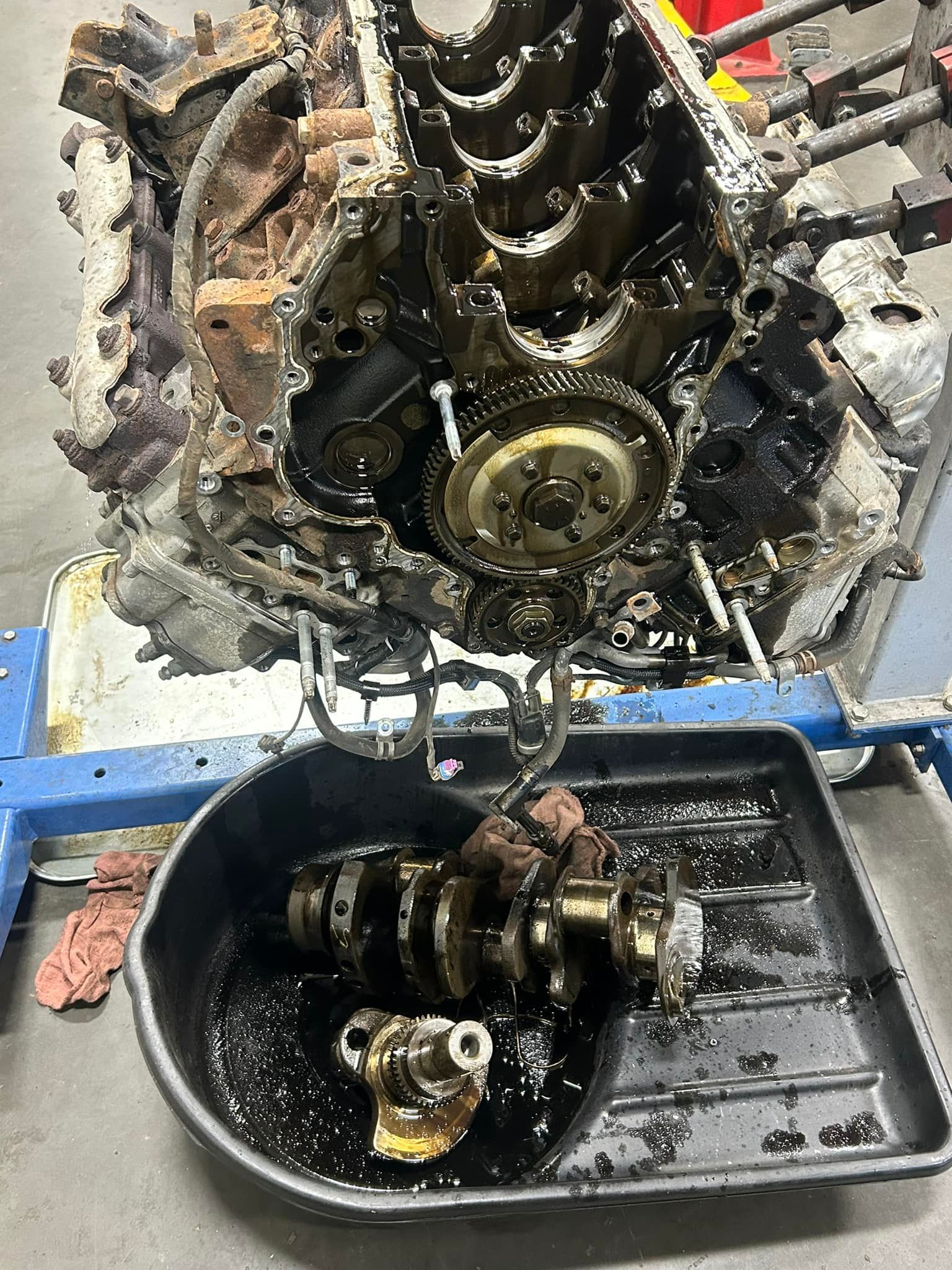 An engine block on a stand with a crankshaft removed and resting in an oil drain pan below.