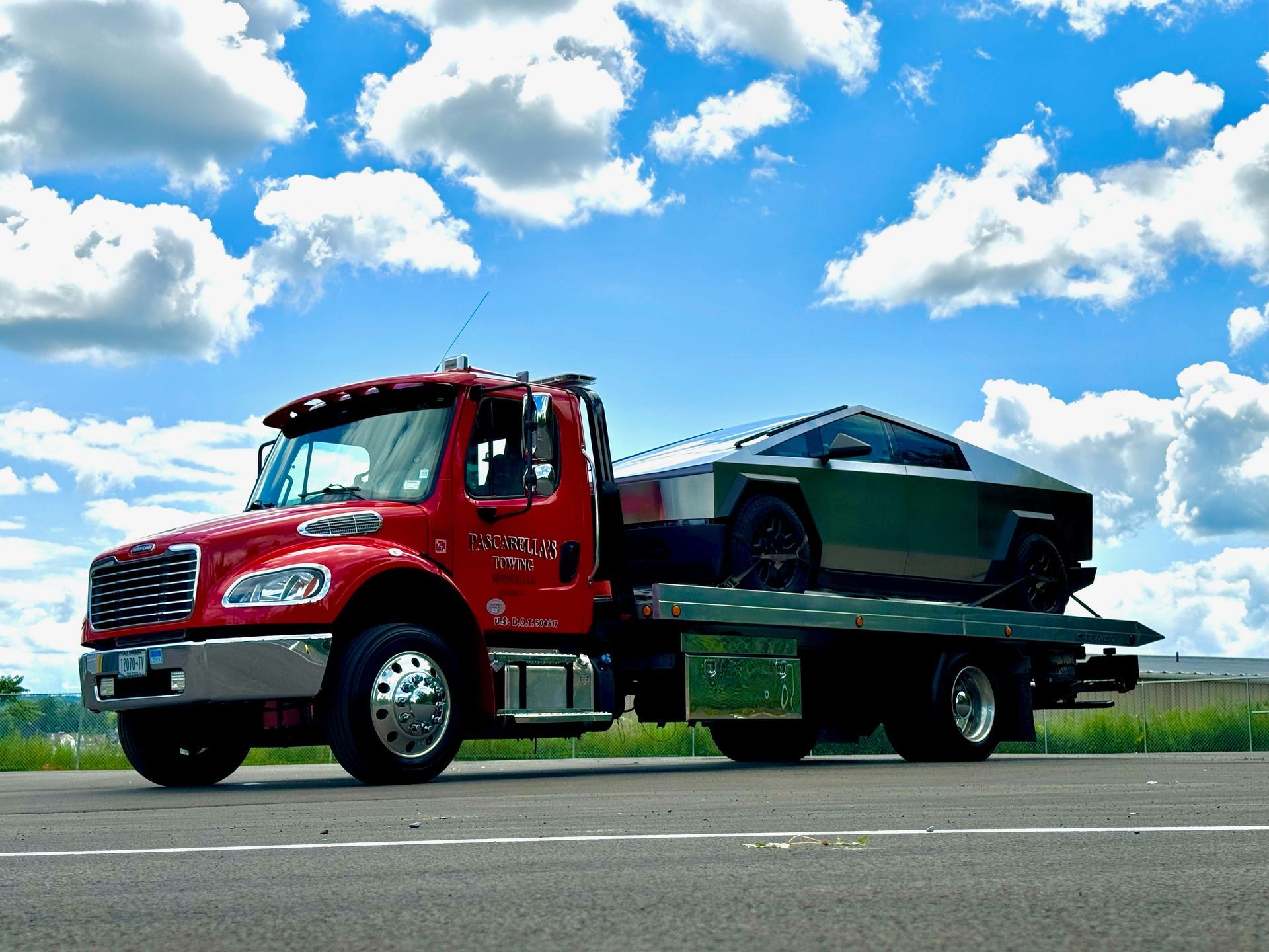 A red tow truck is carrying a grey truck on the back of it.