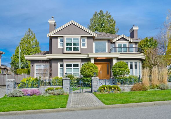 Two-story house with gray exterior, arched windows, and a brick walkway leading to a wooden door.