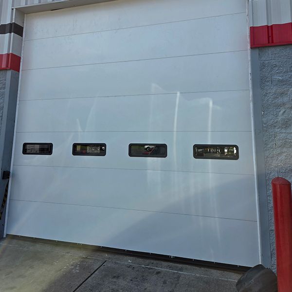 White industrial garage door with four small rectangular windows; red and black trim.