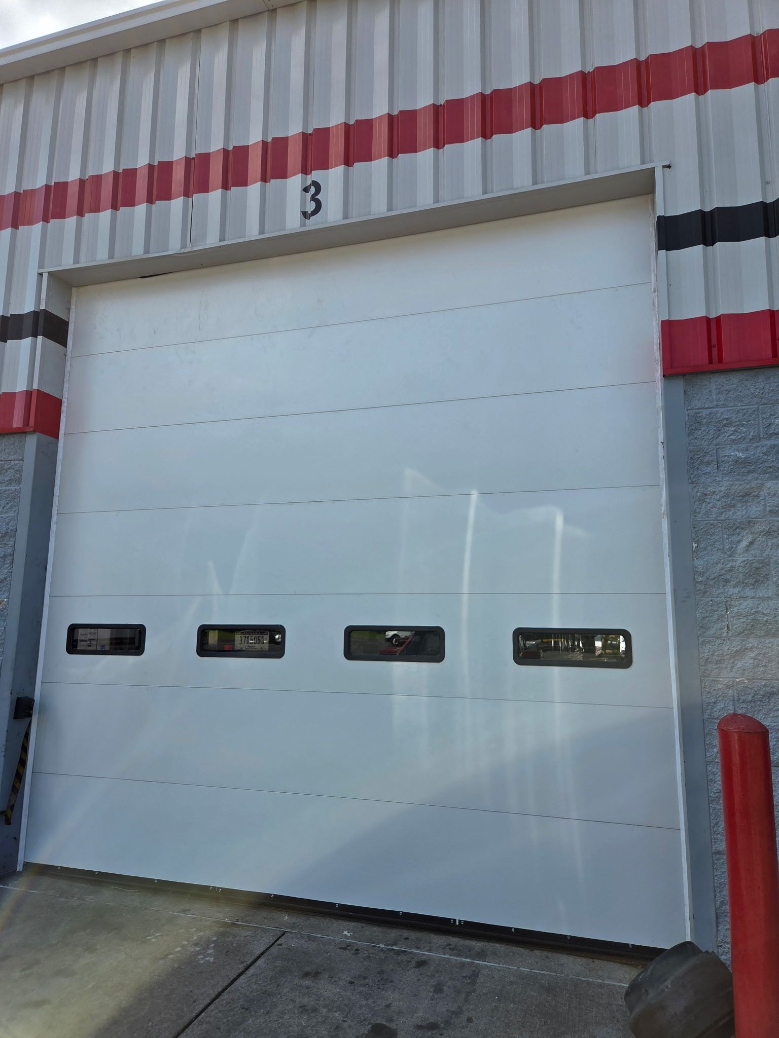 White garage door with number 3 above it; building has red and black stripes along the top.