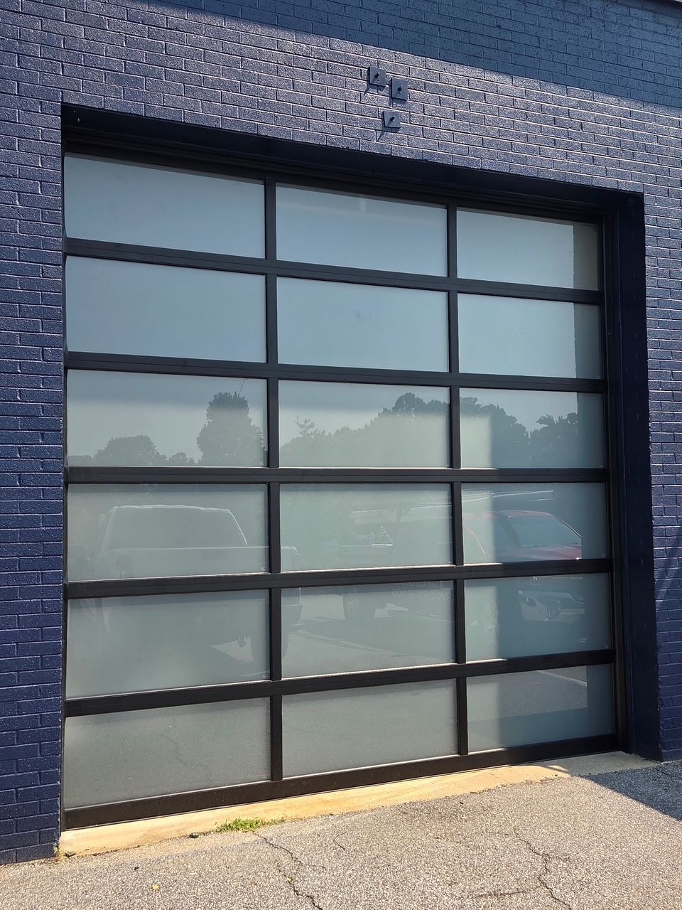 Blue brick building with a modern garage door; black frame and frosted glass panels.
