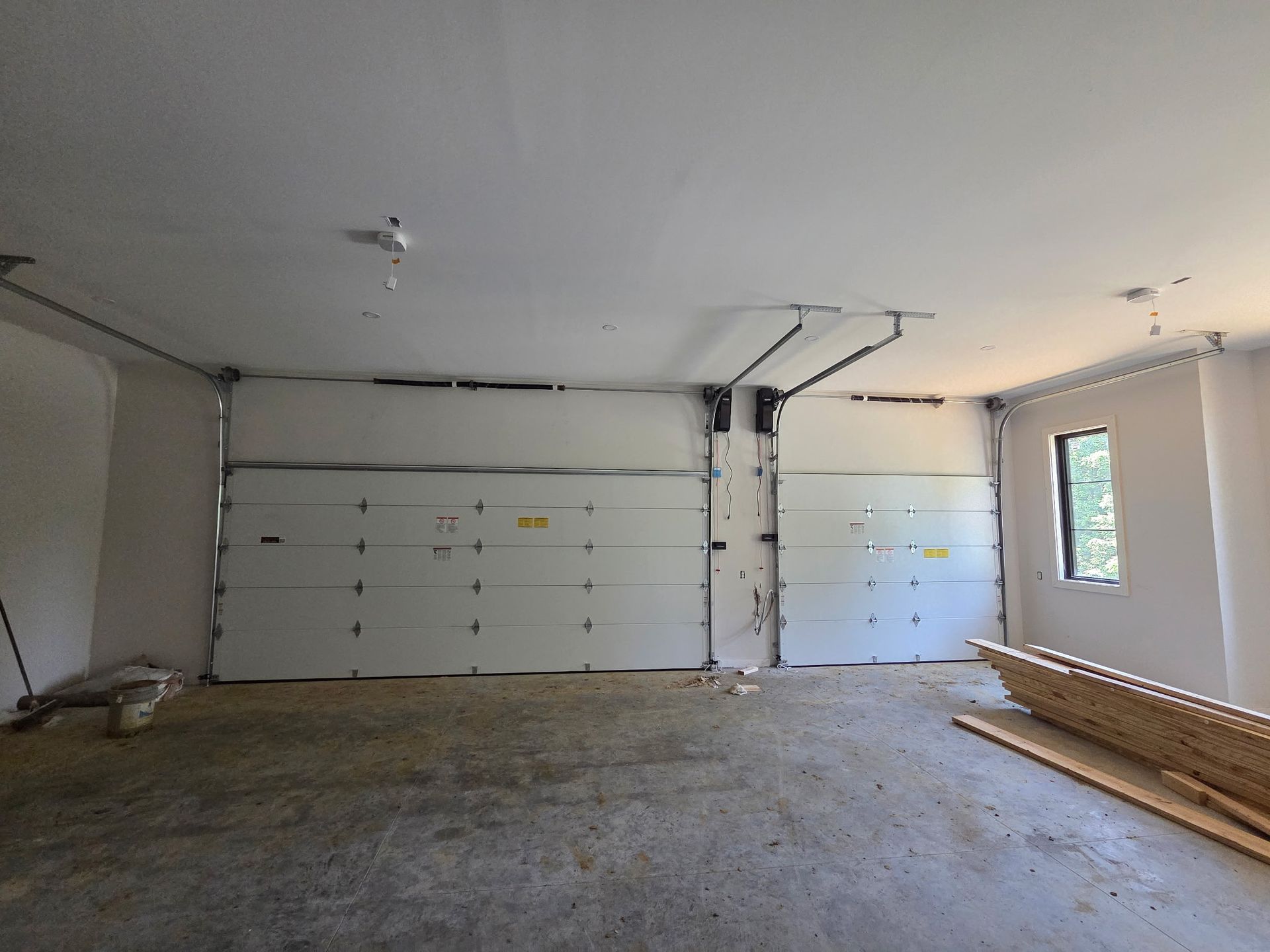 Open garage with two white doors, unfinished interior, construction materials, and natural light.