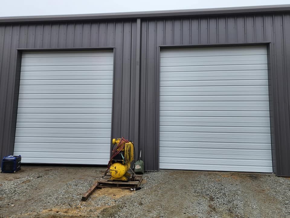 Two closed, white garage doors on a gray metal building. A compressor and generator sit below.