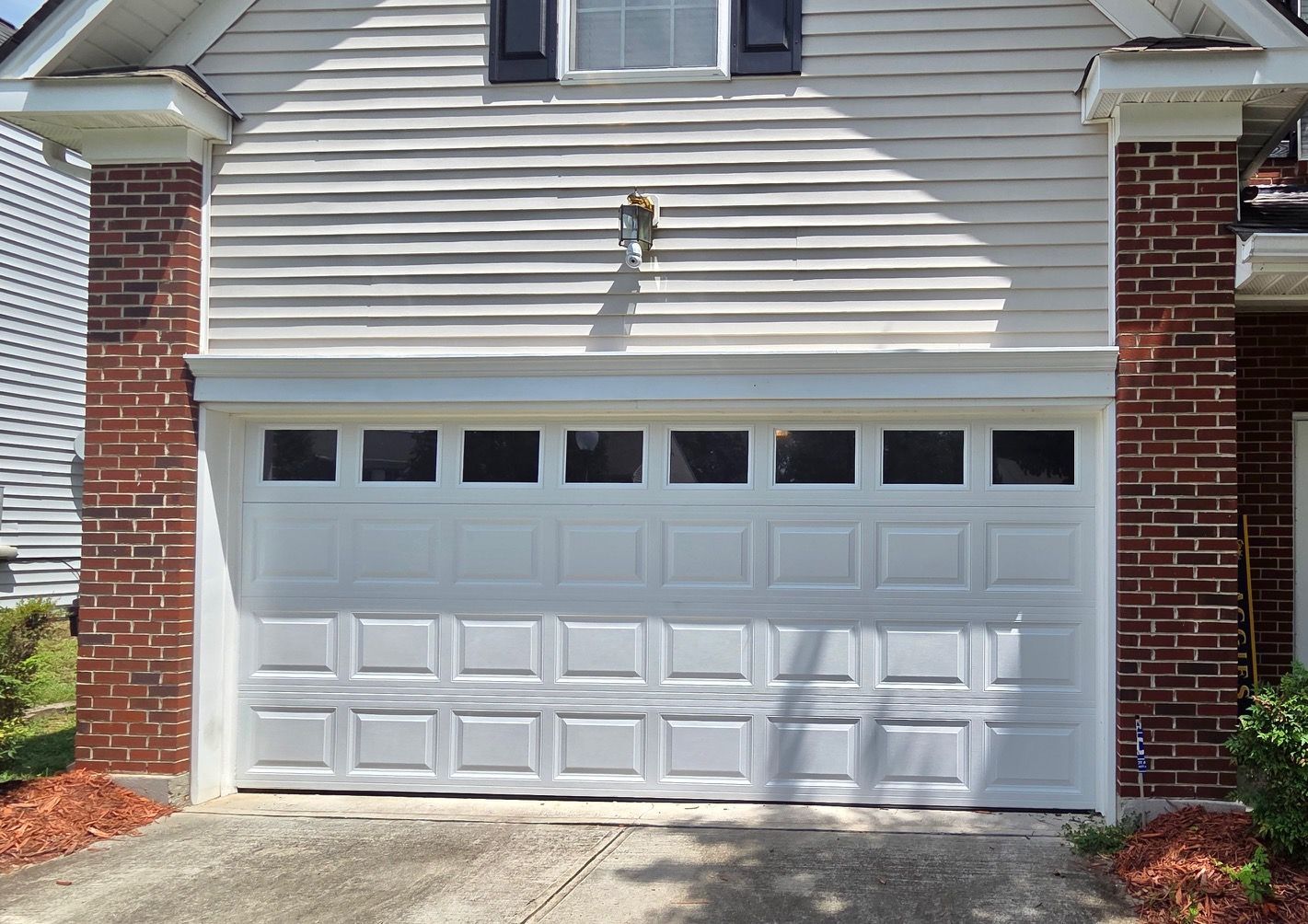 White garage door with windows above, framed by brick columns.