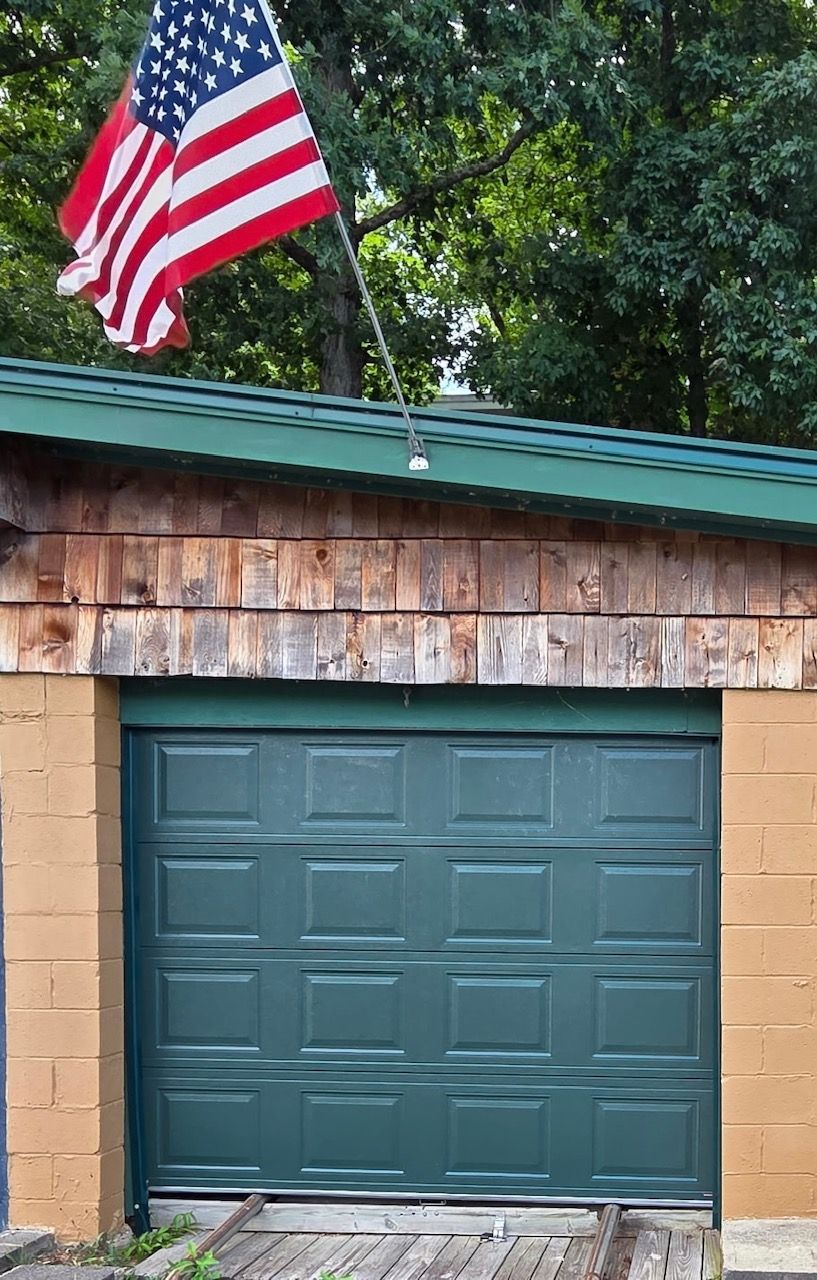 Garage with green door, American flag, and weathered siding.