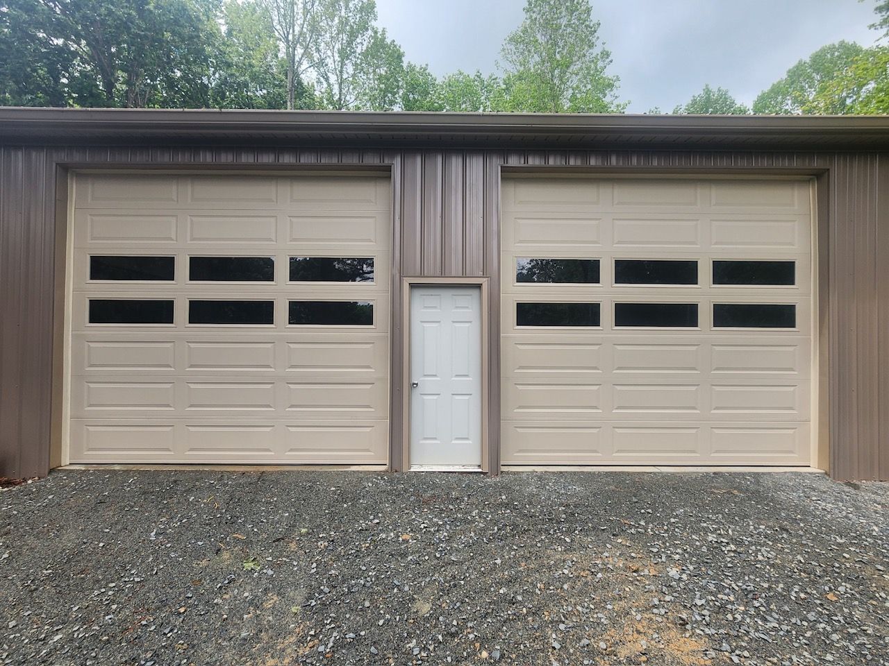 Tan garage with two large doors and a white door centered, on gravel.