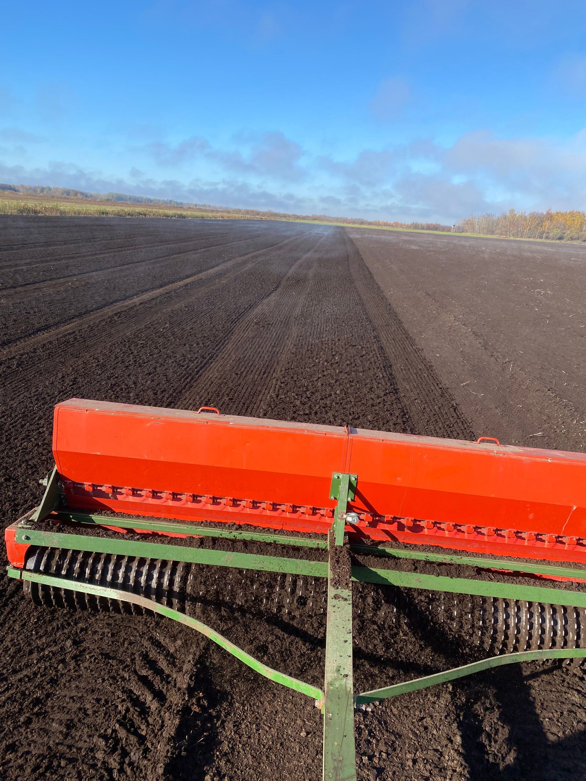 A red farm implement pulled through a dark, freshly tilled field under a blue sky.
