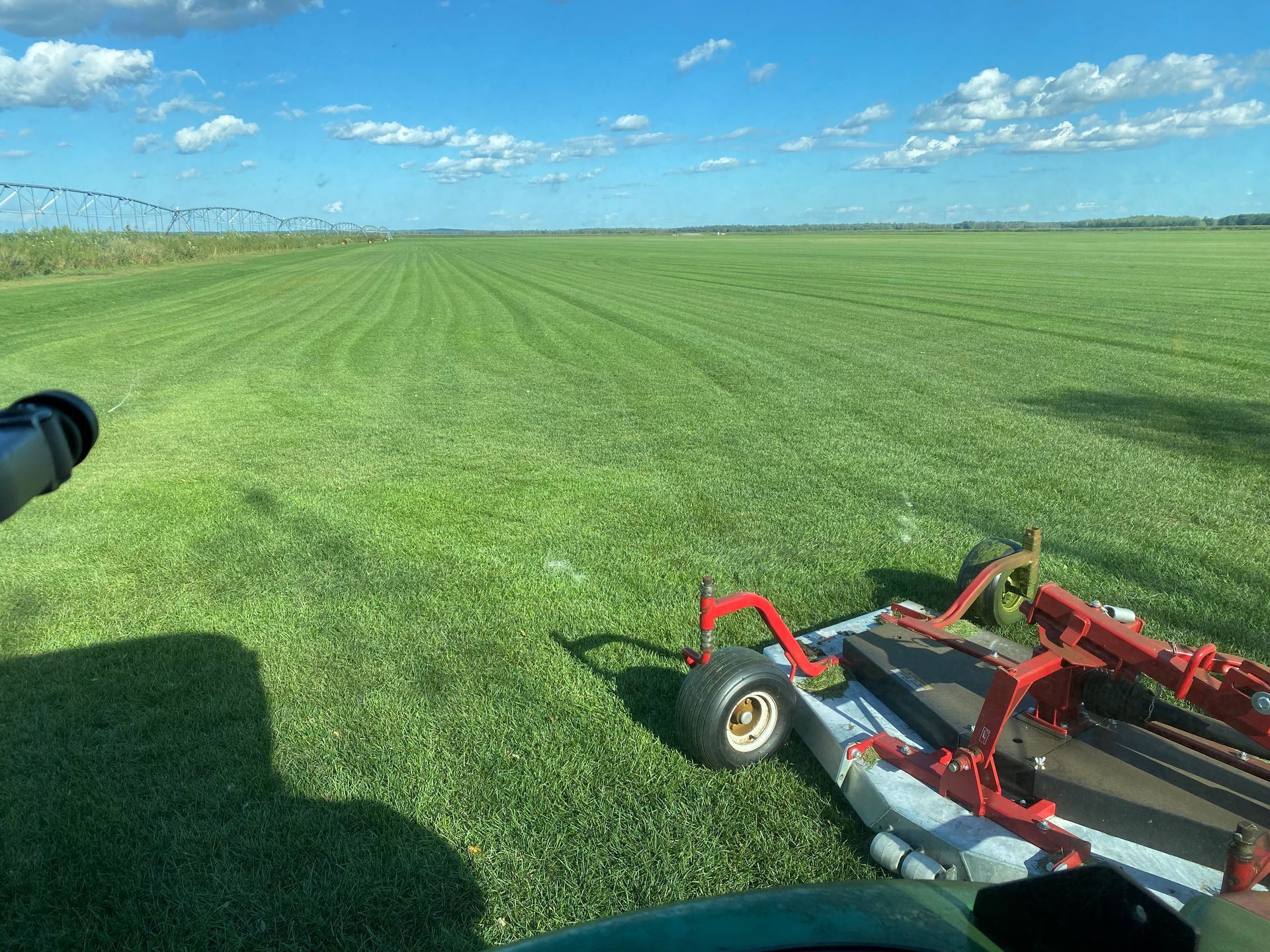A view from a tractor cab looking over a large, freshly mown green field under a clear blue sky.