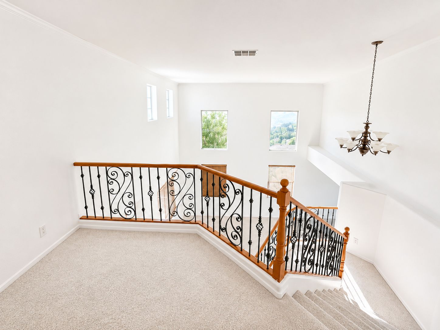 Bright upstairs landing with carpet, wooden railing, white walls, and a chandelier hanging nearby.
