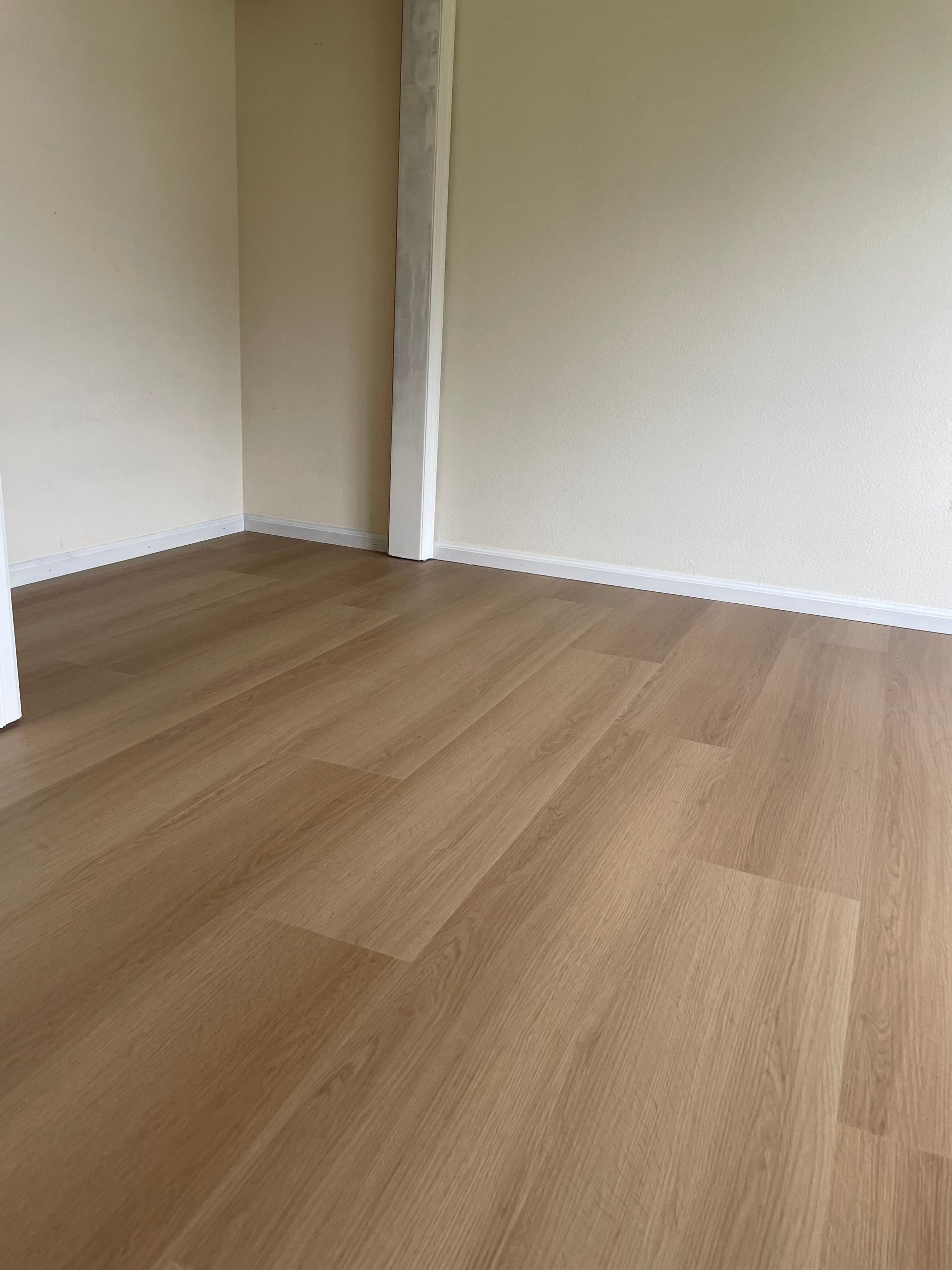 Empty room with light brown wood flooring and beige walls.