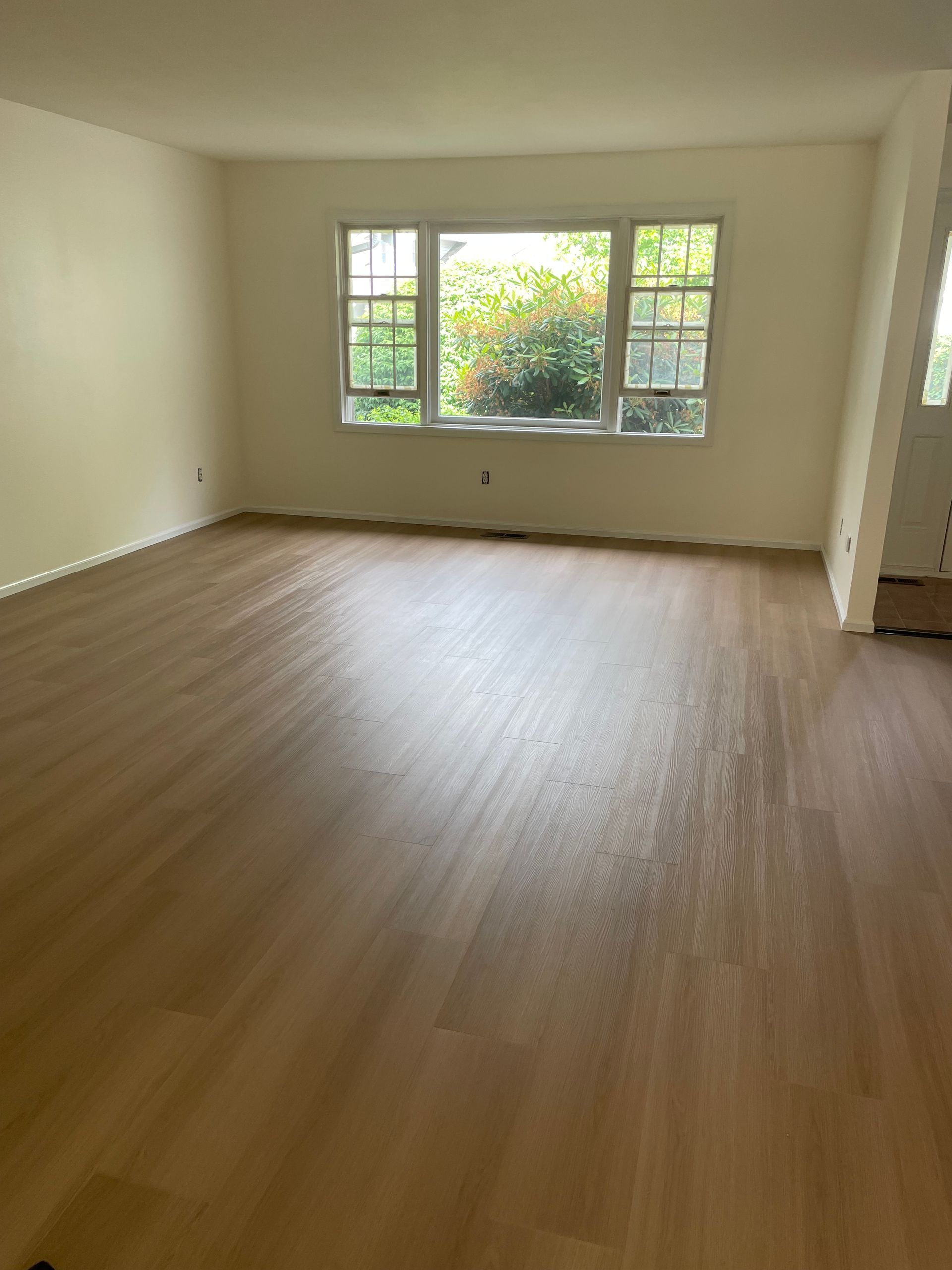 Empty room with light wood floors, a window, and beige walls.