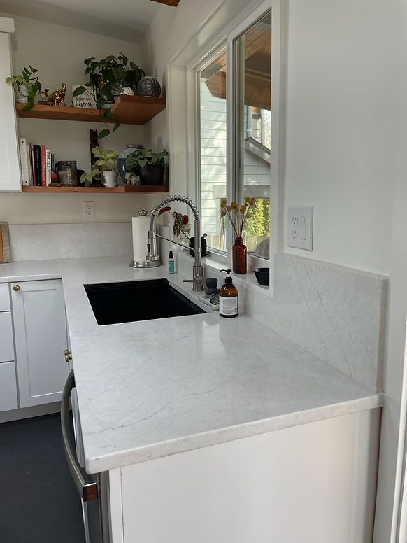A kitchen with white cabinets , a sink , and a window.
