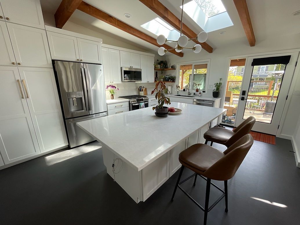 A kitchen with white cabinets , stainless steel appliances , a large island and chairs.
