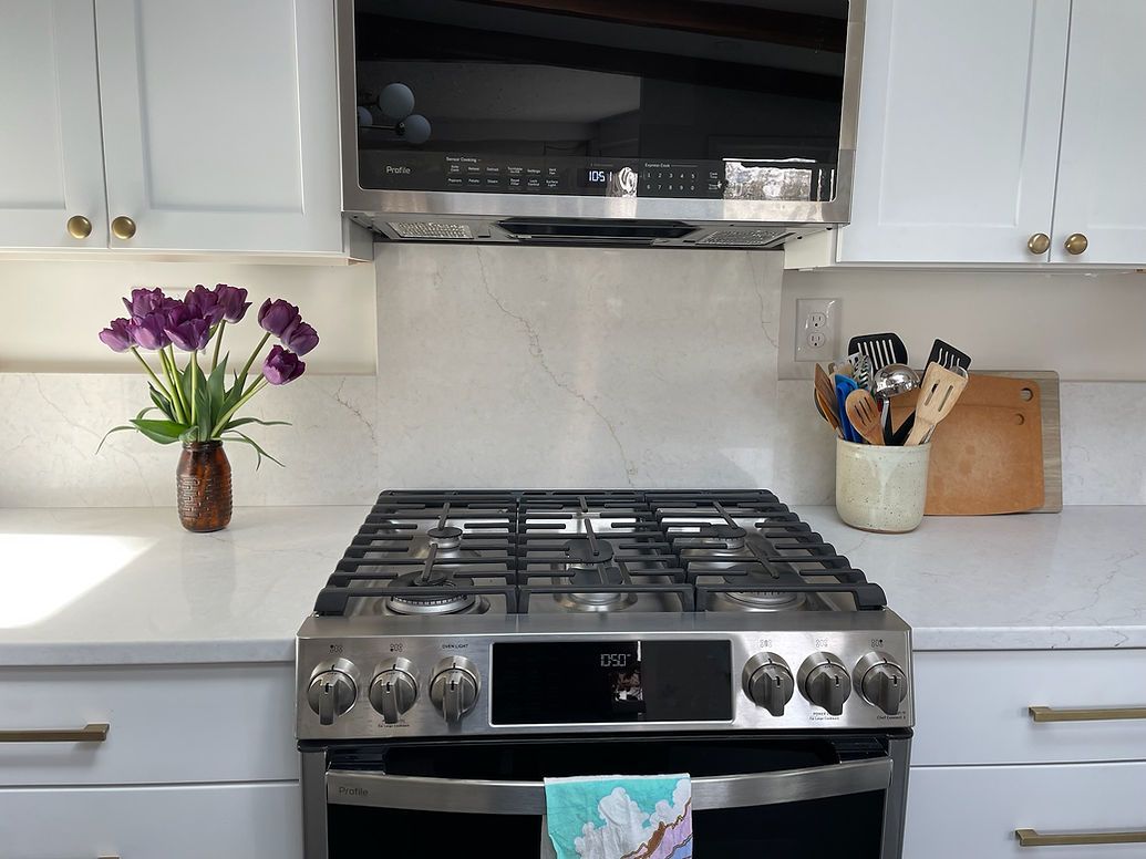 A kitchen with a stove top oven and a vase of purple flowers on the counter.