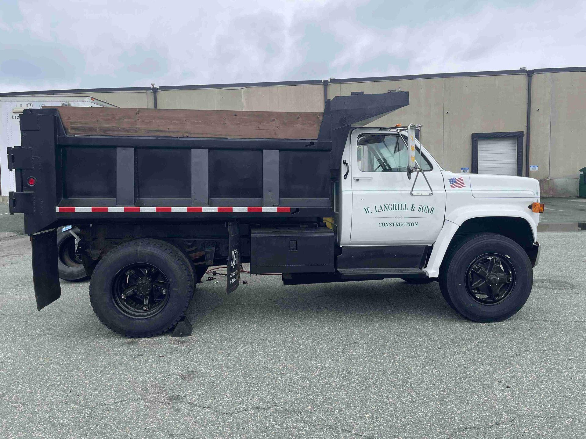 White and black dump truck parked in a lot beside a beige building