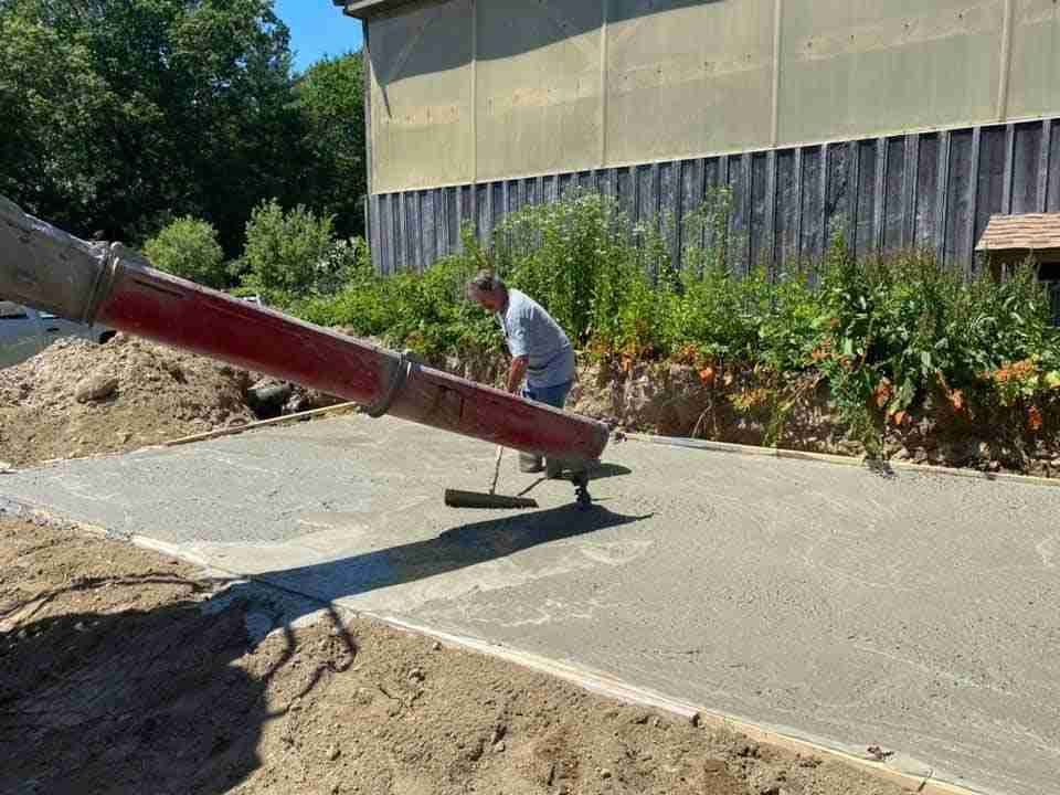 Worker pushing a red concrete chute on a sunny construction site beside a building