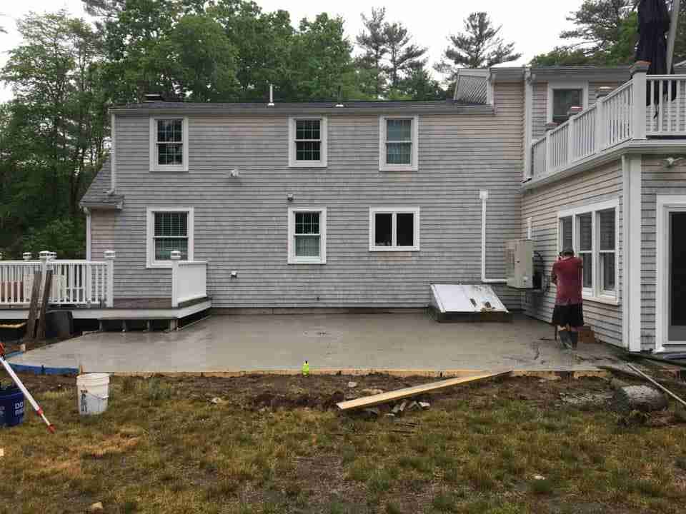 Gray house with a wooden deck and one person standing by the door in the backyard.