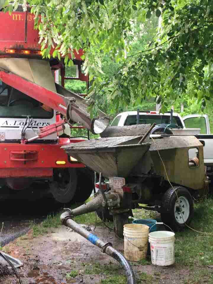 Red concrete mixer by a truck, with buckets and a hose in a muddy outdoor work area