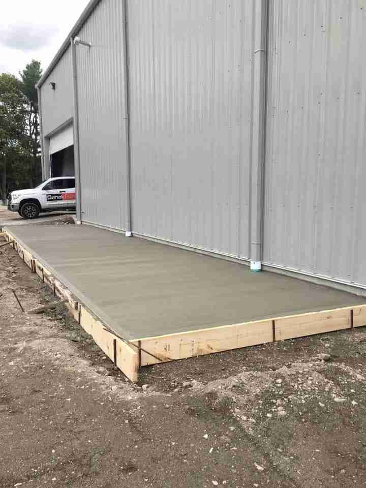 Concrete loading dock ramp beside a gray metal warehouse, with a white truck partially visible.