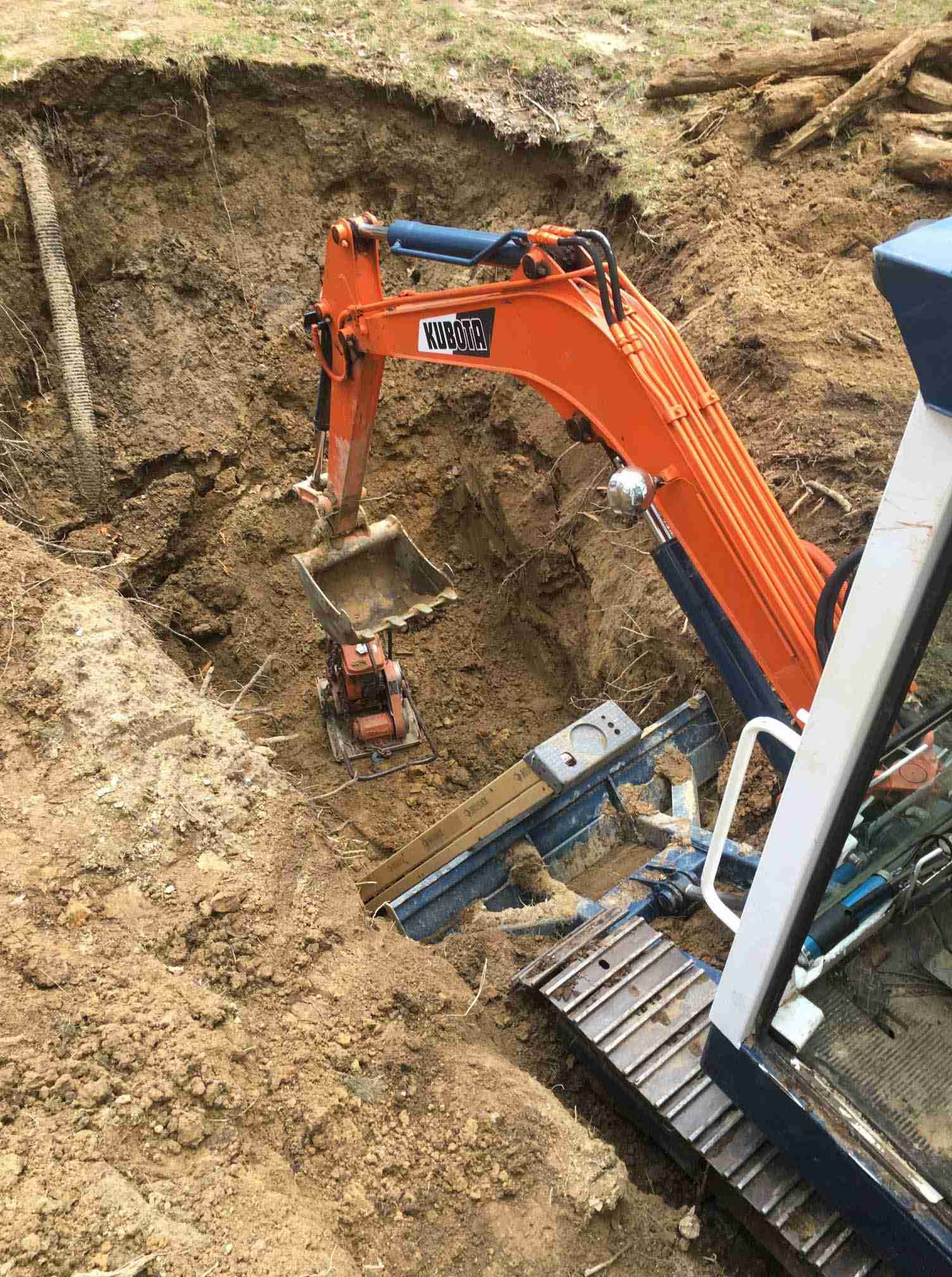 Orange excavator digging into a dirt hillside beside a construction site