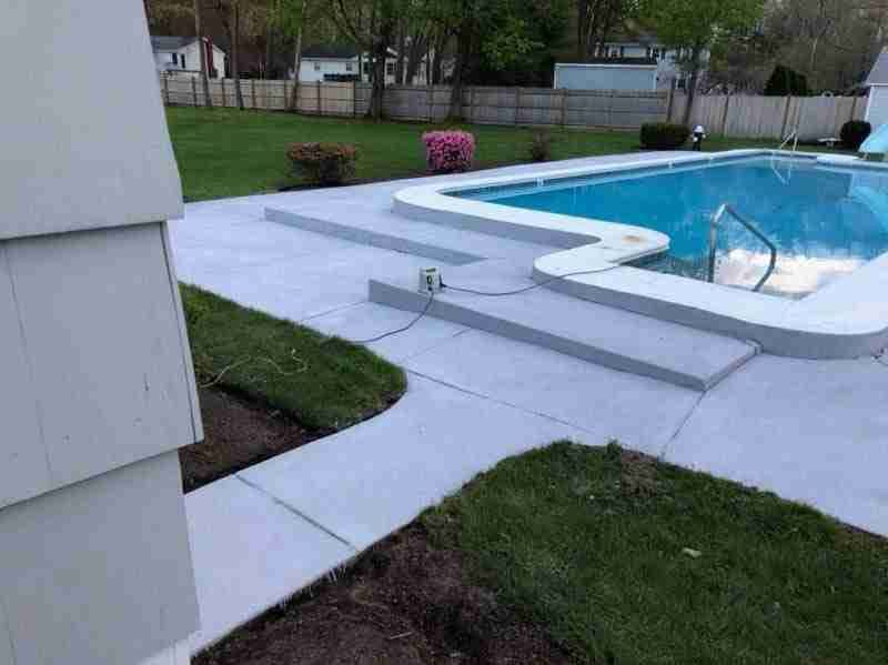 Backyard pool with white concrete patio, green lawn, and a raised spa with water jets.
