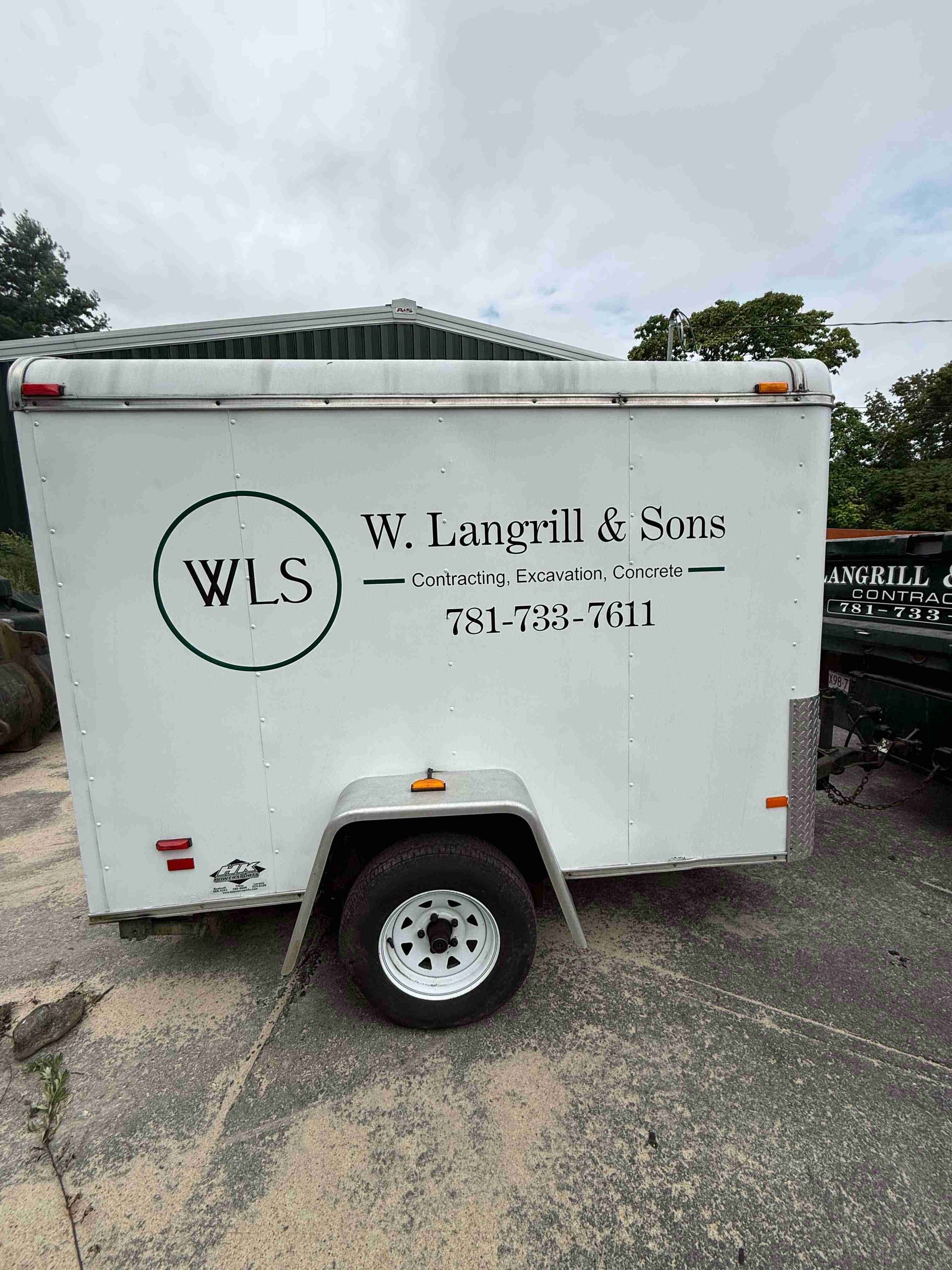 White utility trailer with W.L. Langill & Sons logo and text parked on wet pavement under cloudy sky