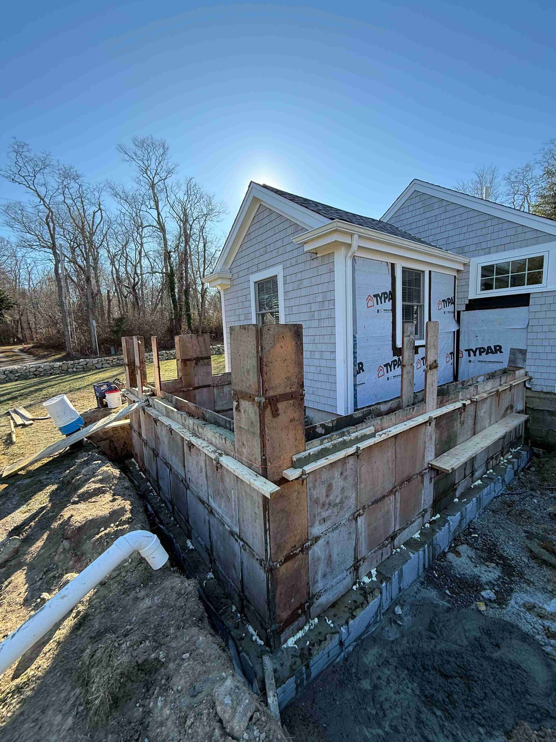 Partially built small white house with brick foundation, exposed framing, and construction debris on a sunny lot
