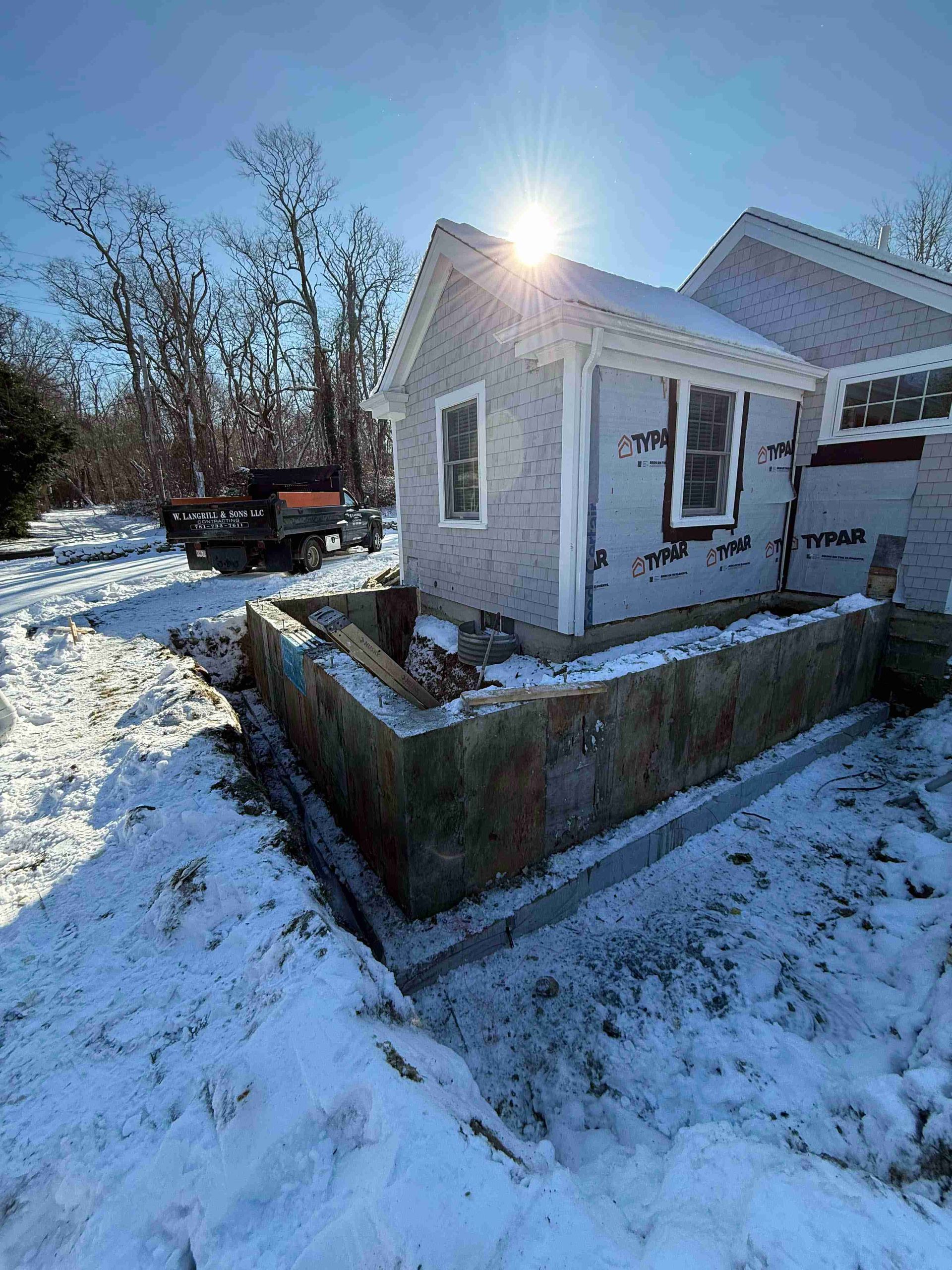 Snowy backyard with a small white house addition and bright sun overhead