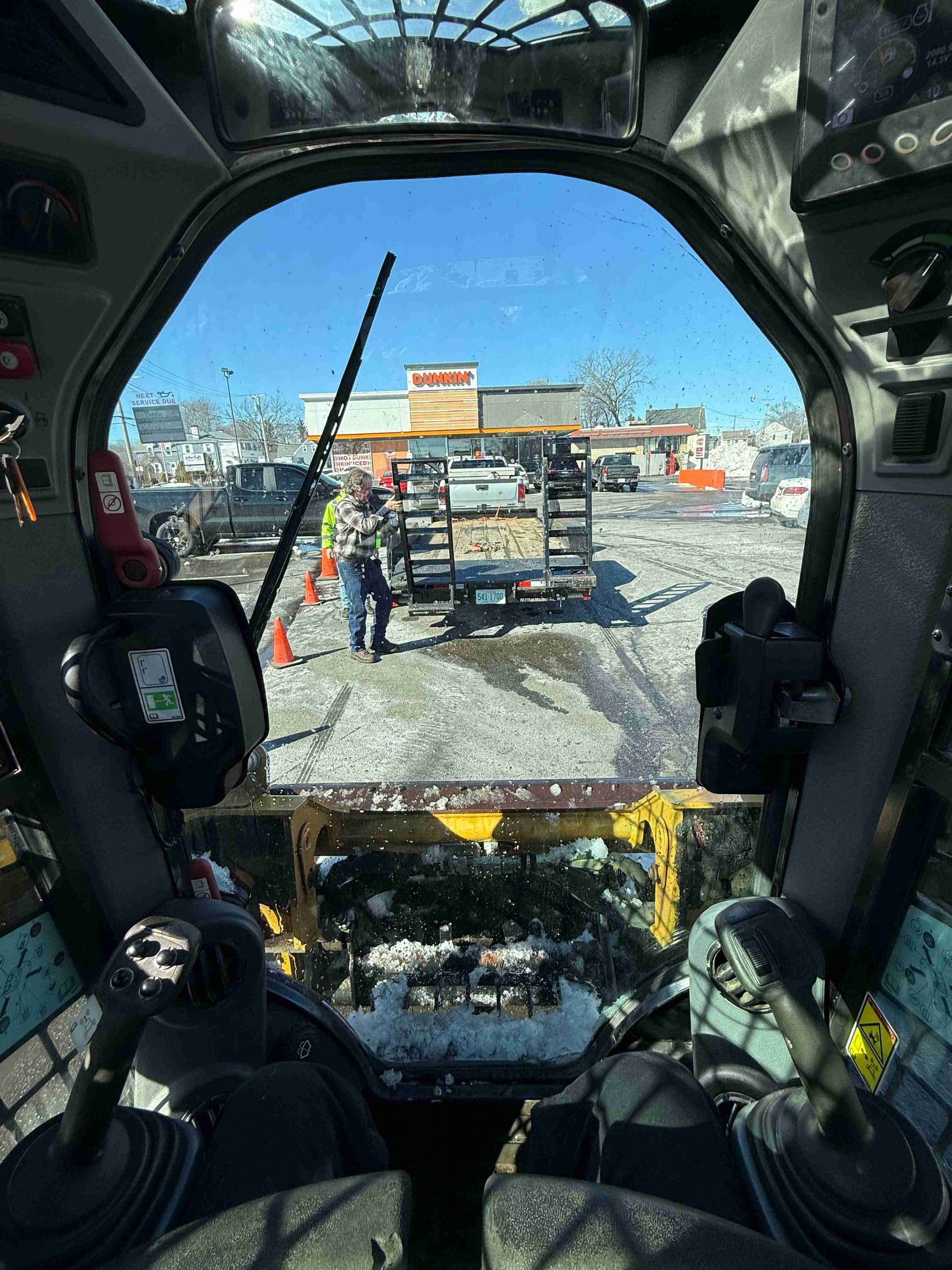 Snowy view through a vehicle cab windshield toward a loaded truck ahead.