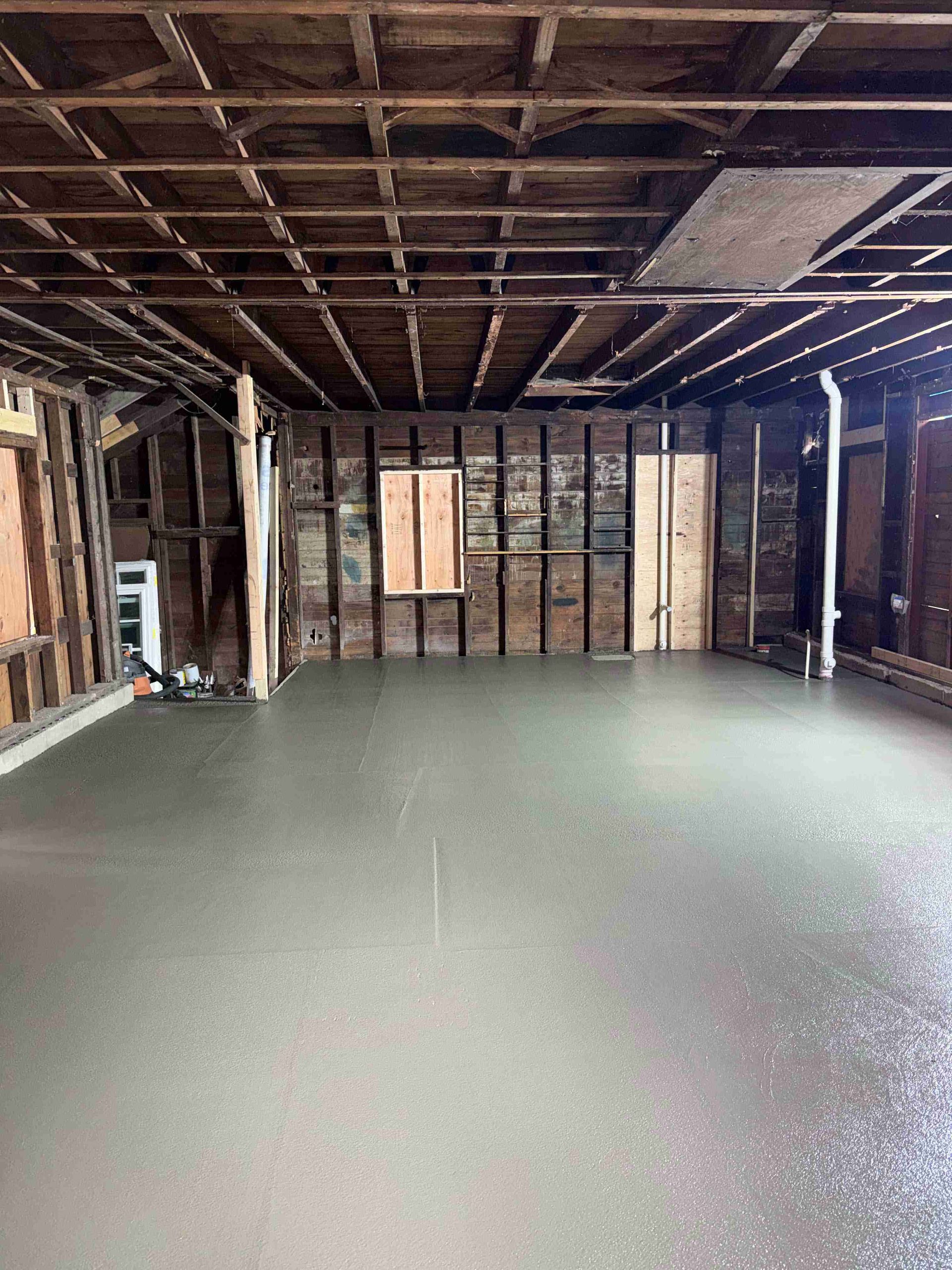 Empty unfinished room with exposed wooden ceiling and fresh gray concrete floor