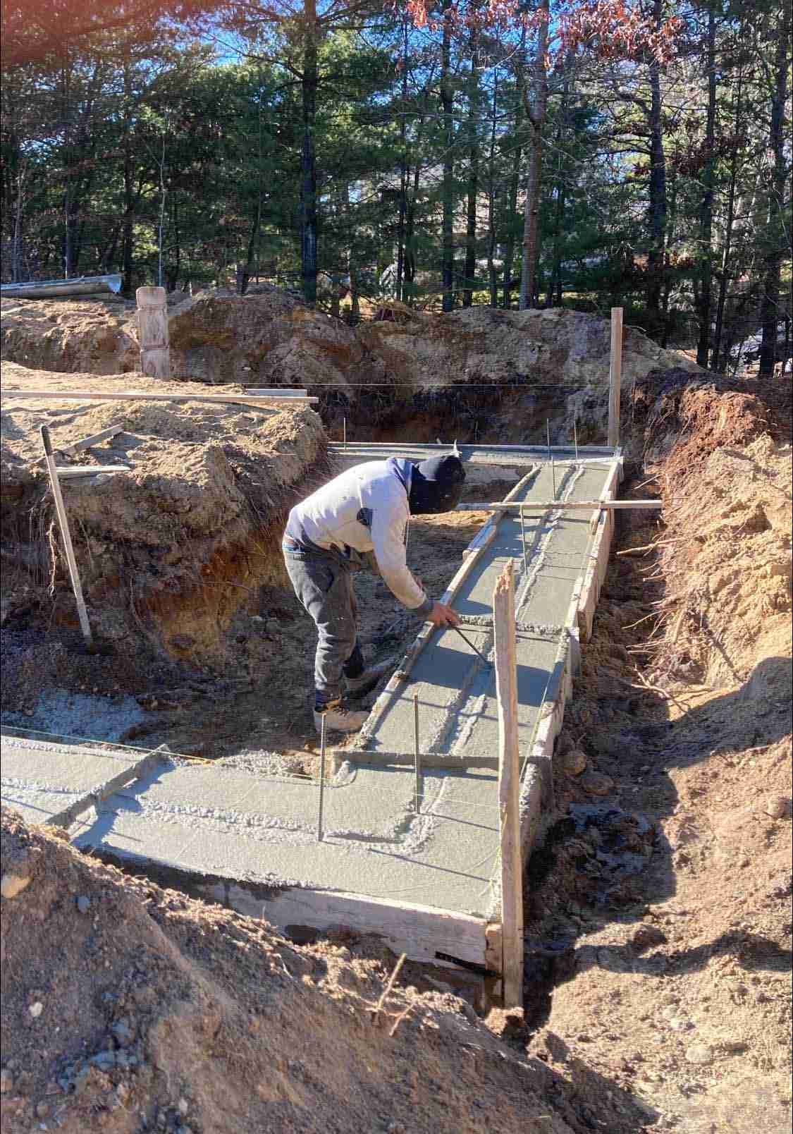 Worker smoothing wet concrete on a sloped construction form in a dirt excavation area.