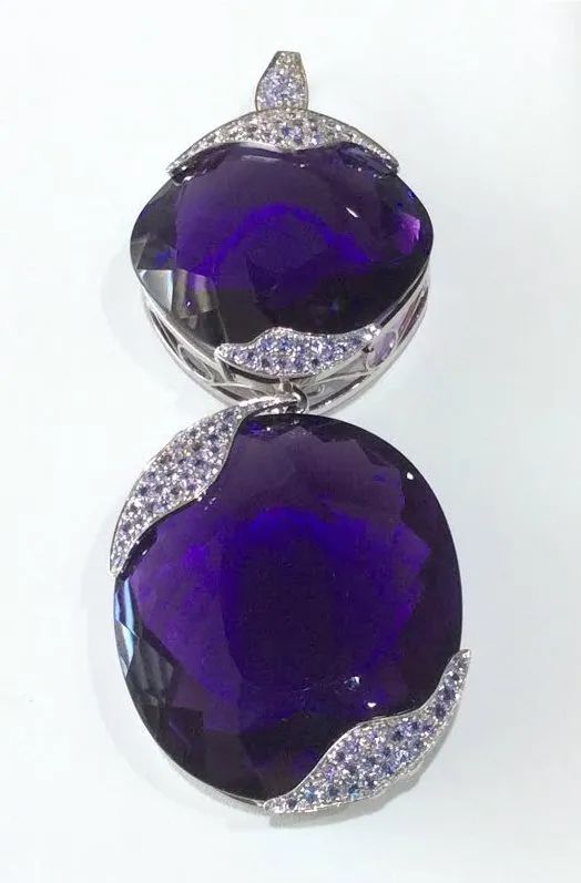 a pendant with two purple stones and diamonds on a white surface