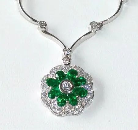a necklace with a flower shaped pendant with emeralds and diamonds