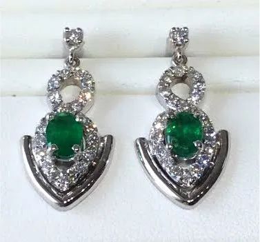 a pair of emerald and diamond earrings are sitting on a white surface