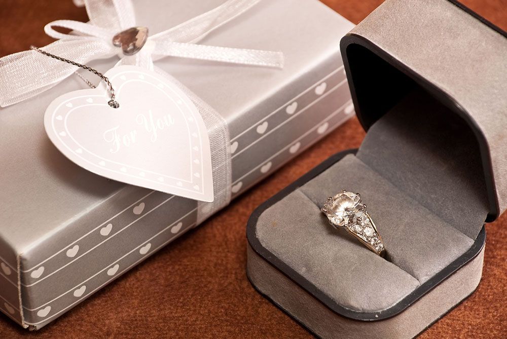 a diamond ring in a box next to a gift box.