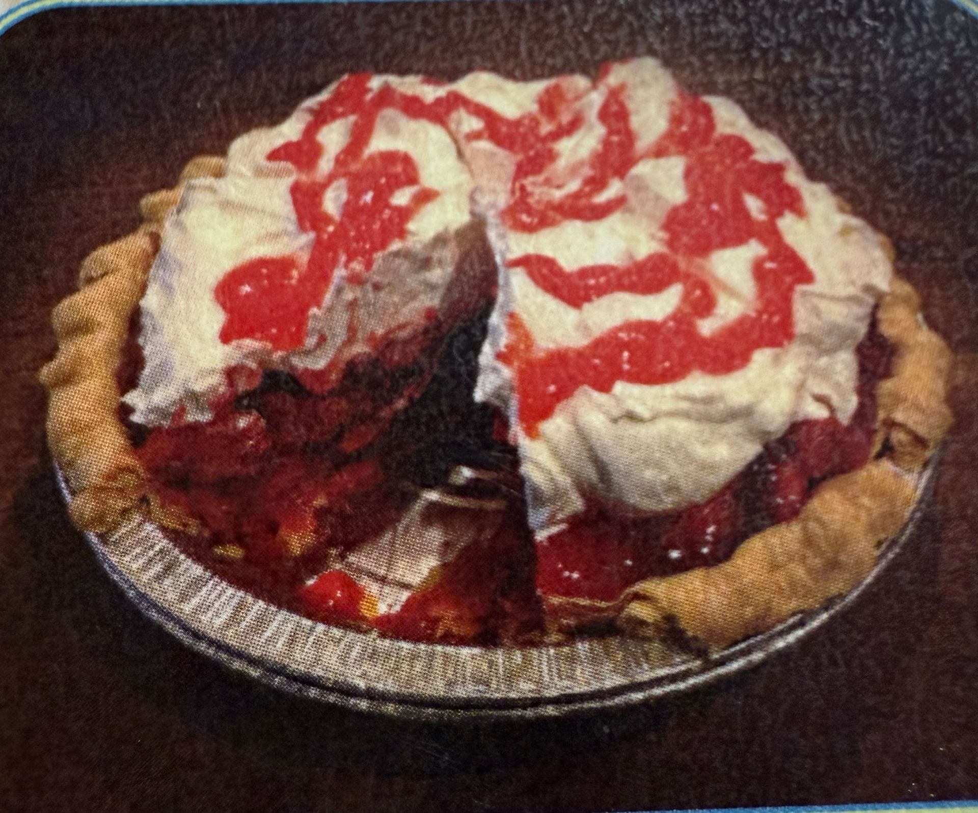 Slice of cherry pie with whipped cream and red drizzle on a foil-lined pie plate